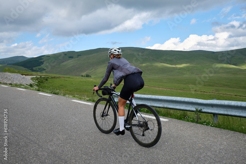 Fit female cyclist wearing cycling kit and helmet riding on the road on a gravel bike. Empty mountain road. Sports motivation image. Bucegi Mountains