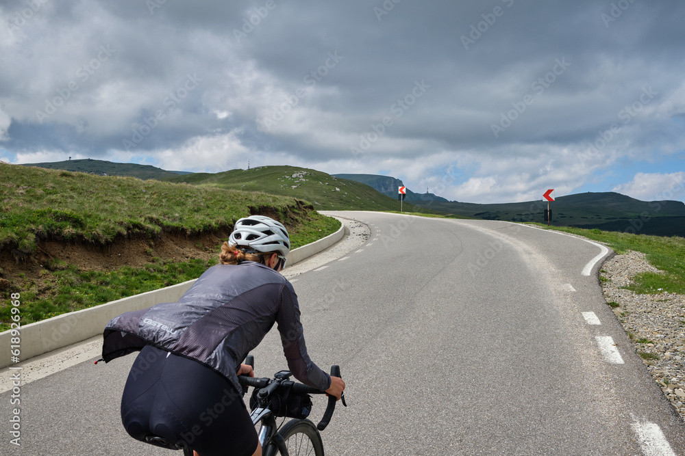 Obraz premium Woman cyclist riding a road bike with a view of the mountains. Sport motivation.Female cyclist wearing a cycling kit and helmet.Bucegi Mountains