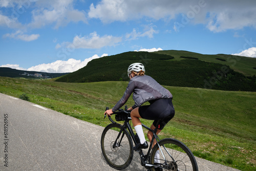 Woman cyclist riding a road bike with a view of the mountains. Sport motivation.Female cyclist wearing a cycling kit and helmet.Bucegi Mountains photo