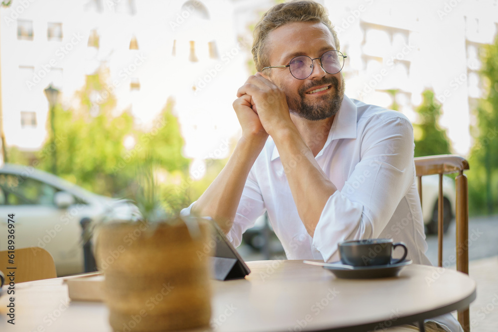 Happy and stylish blond man enjoying moment of relaxation in an outdoor caffe. With a cup of coffee in hand, he exudes a sense of joy and contentment. . High quality photo Happy and stylish blond man enjoying moment of relaxation in an outdoor caffe. With a cup of coffee in hand, he exudes a sense of joy and contentment. . High quality photo