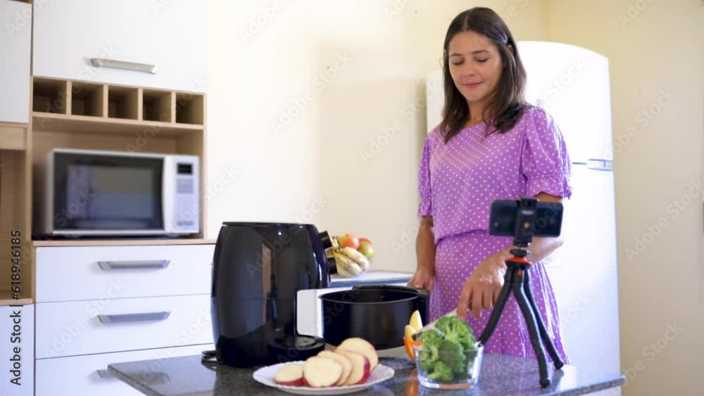 Woman using the air fryer to fry food in her home kitchen while watching a video tutorial teaching the recipe for the dish Woman using the air fryer to fry food in her home kitchen while watching a video tutorial teaching the recipe for the dish