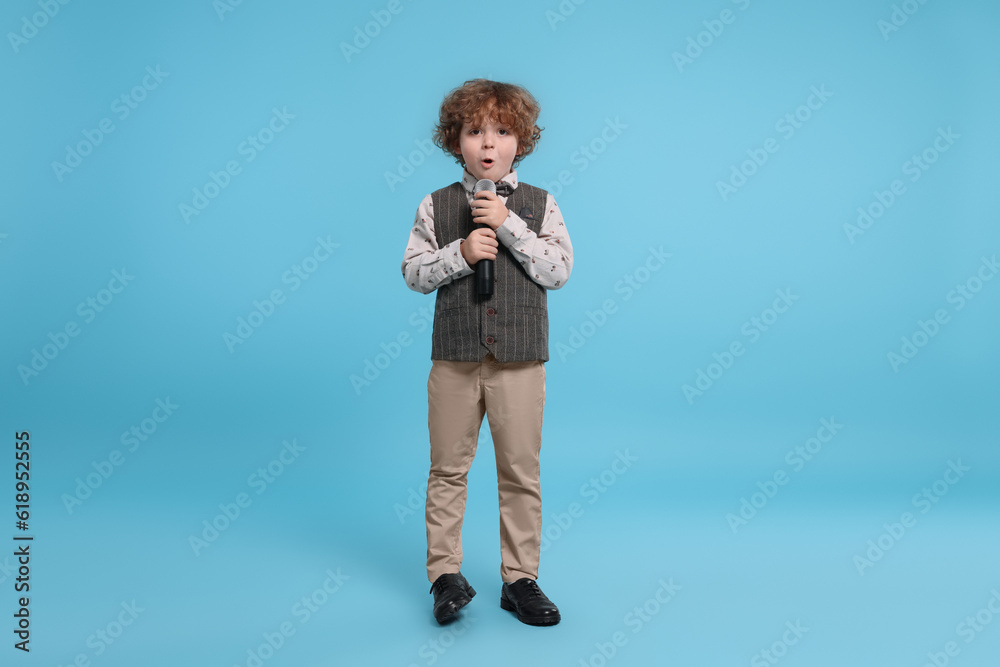 Cute little boy with microphone singing on light blue background Cute little boy with microphone singing on light blue background