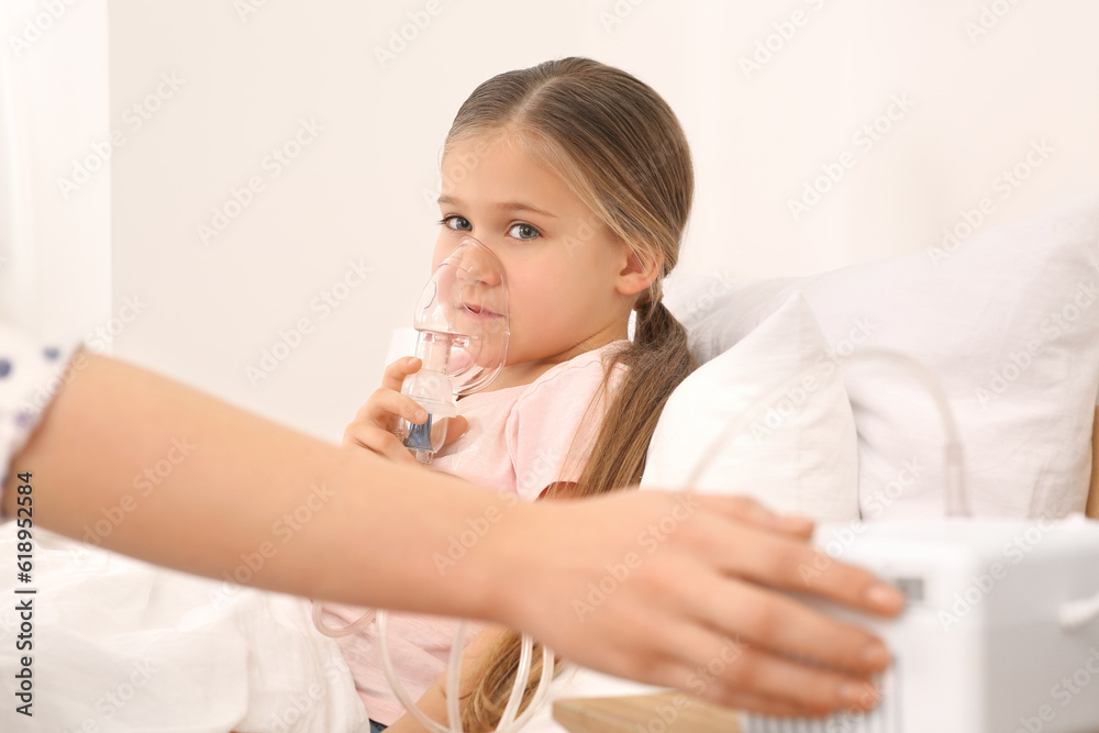 Mother helping her sick daughter with nebulizer inhalation in bedroom, closeup Mother helping her sick daughter with nebulizer inhalation in bedroom, closeup