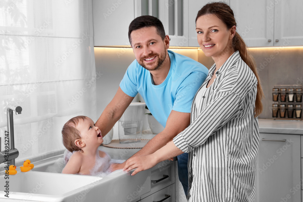 Fototapeta premium Father and mother washing their little baby in sink at home