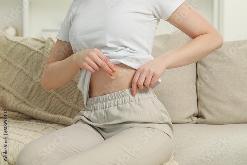 Woman applying contraceptive patch onto her body on sofa, closeup