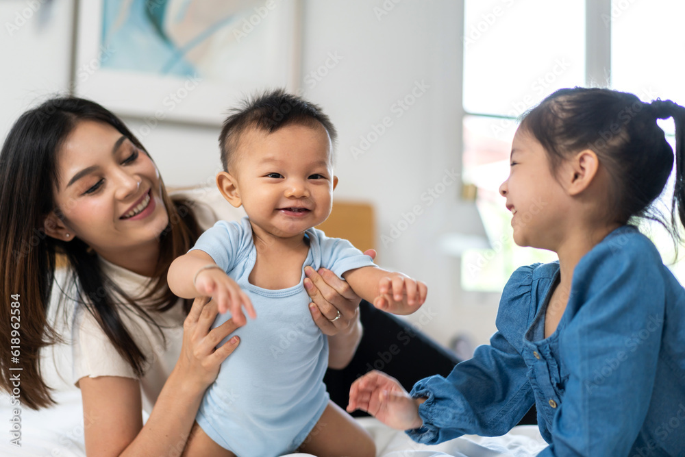 Portrait of enjoy happy love family asian mother playing with adorable little asian baby and sister girl, newborn, infant.Mom touching care with cute son in a white bedroom.Love of family concept Portrait of enjoy happy love family asian mother playing with adorable little asian baby and sister girl, newborn, infant.Mom touching care with cute son in a white bedroom.Love of family concept