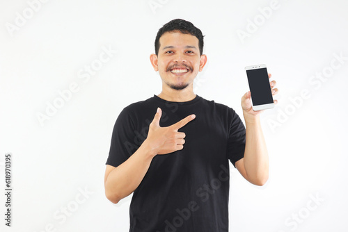 Adult Asian man smiling happy while showing blank mobile phone screen and pointing on it photo