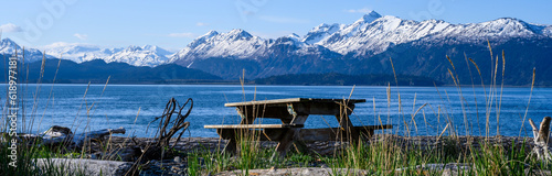 Foto Wood picnic table on the on beach of Katchemak Bay on a sunny summer day, mounta