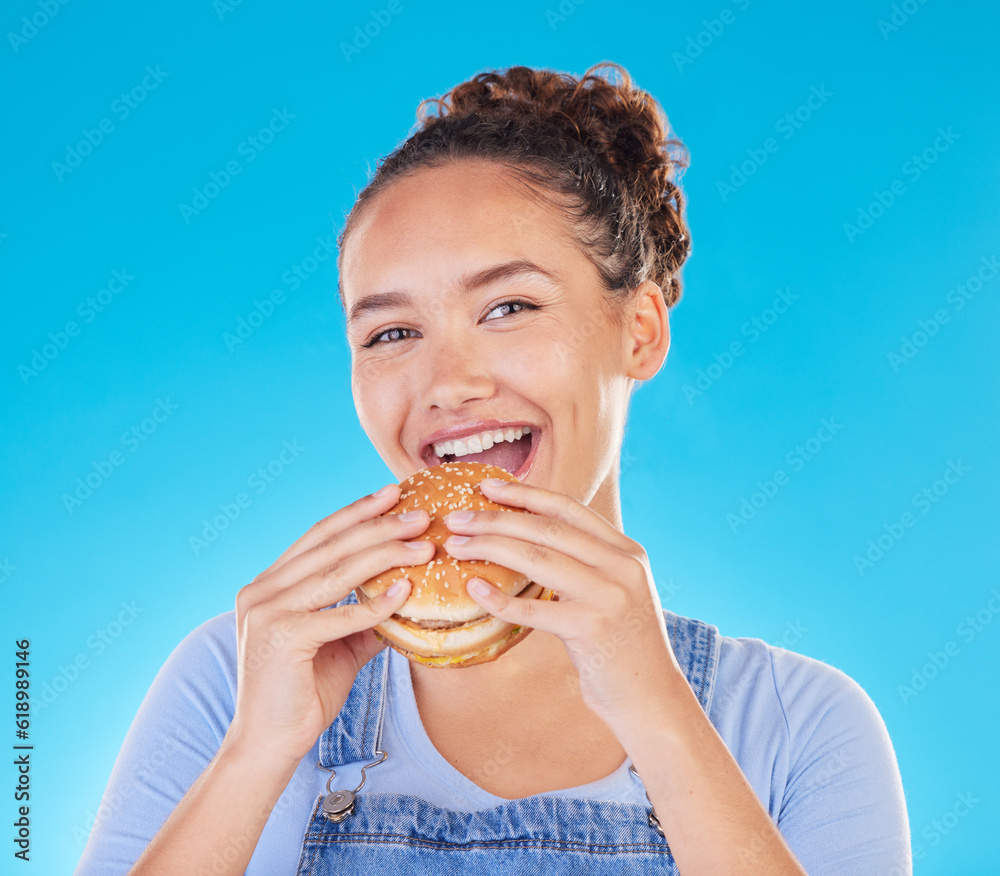 Burger, smile and woman eating fast food and happy with lunch meal with a smile isolated in a studio blue background. Breakfast, craving and portrait of young female person enjoy snack or sandwich Burger, smile and woman eating fast food and happy with lunch meal with a smile isolated in a studio blue background. Breakfast, craving and portrait of young female person enjoy snack or sandwich