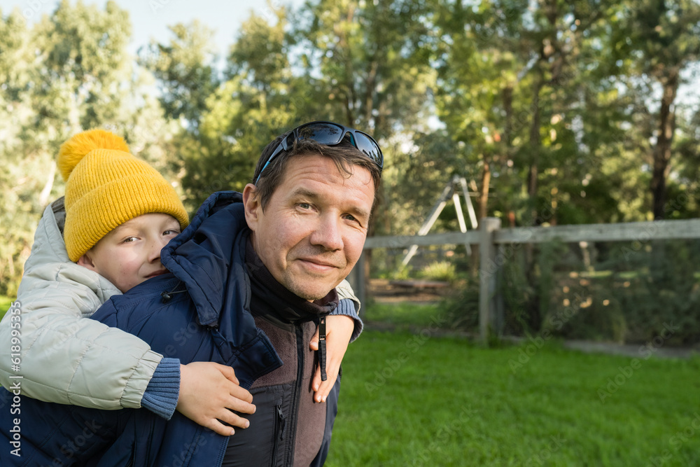 Father giving his son a piggyback ride outdoors. Lifestyle portrait, copy space. Autumn.
