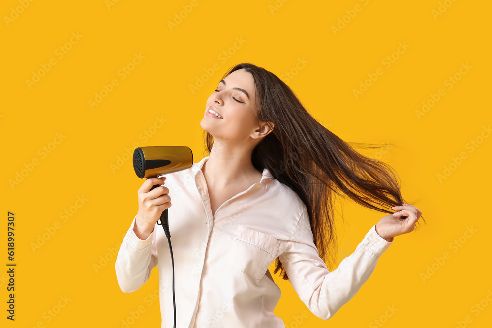 Beautiful young woman with hair dryer on yellow background Beautiful young woman with hair dryer on yellow background