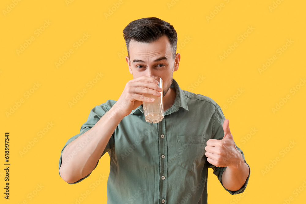 Young man with dissolved tablet and glass of water on yellow background Young man with dissolved tablet and glass of water on yellow background