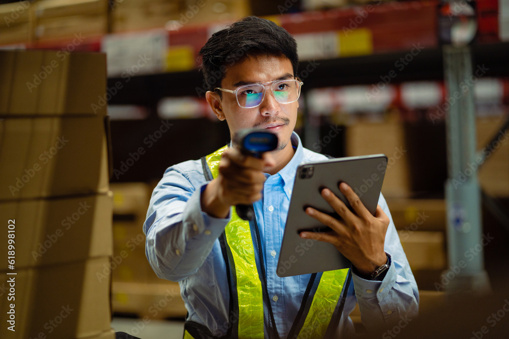 Asian male worker in security suit with tablet computer looking for items in a large warehouse. Logistics and export business Factory warehouse. business Industrial. warehouse. Asian male worker in security suit with tablet computer looking for items in a large warehouse. Logistics and export business Factory warehouse. business Industrial. warehouse.