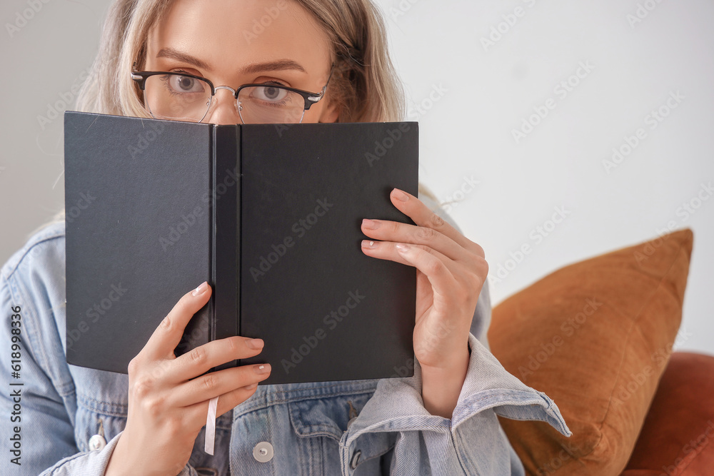 Obraz premium Young woman in glasses peeking over black book, reading and learning concept, education and knowledge acquisition