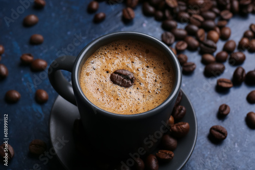 Cup of hot espresso and coffee beans on blue background