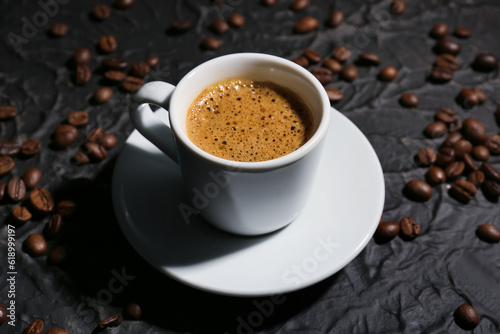 Cup of hot espresso and coffee beans on black background