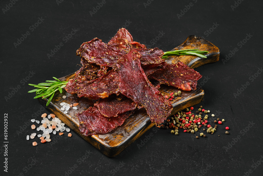 Dried beef jerky slices on wooden board with salt and pepper. Dried beef jerky slices on wooden board with salt and pepper.