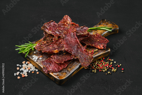 Fotografía Dried beef jerky slices on wooden board with salt and pepper.