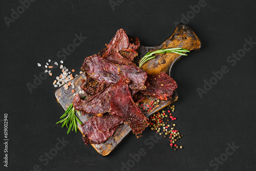 Overhead view of dried beef jerky slices on wooden board with salt and pepper