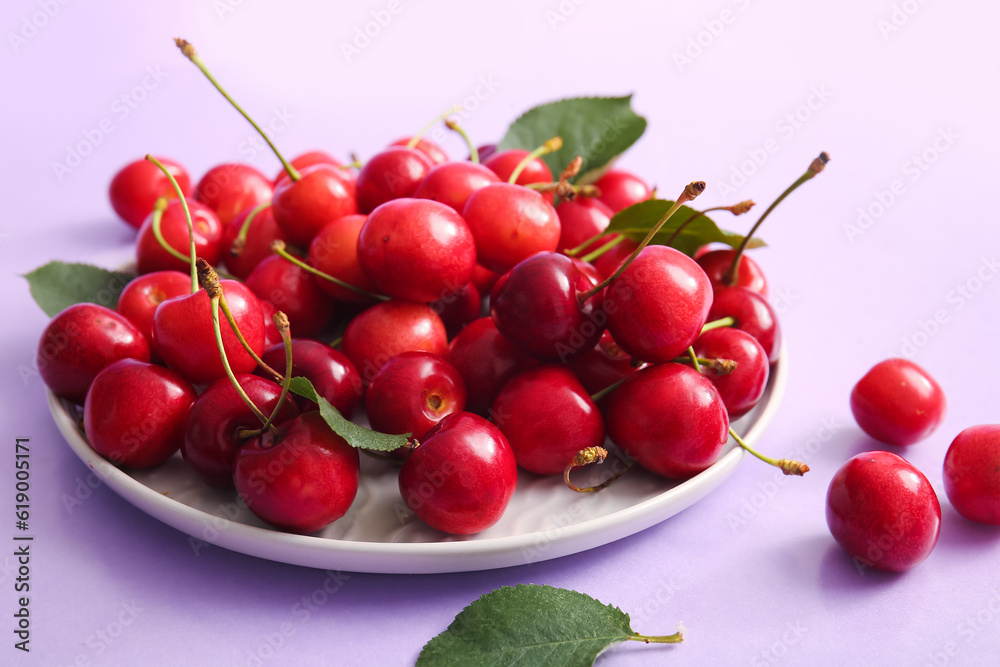 Plate of sweet cherries and leaves on lilac background Plate of sweet cherries and leaves on lilac background
