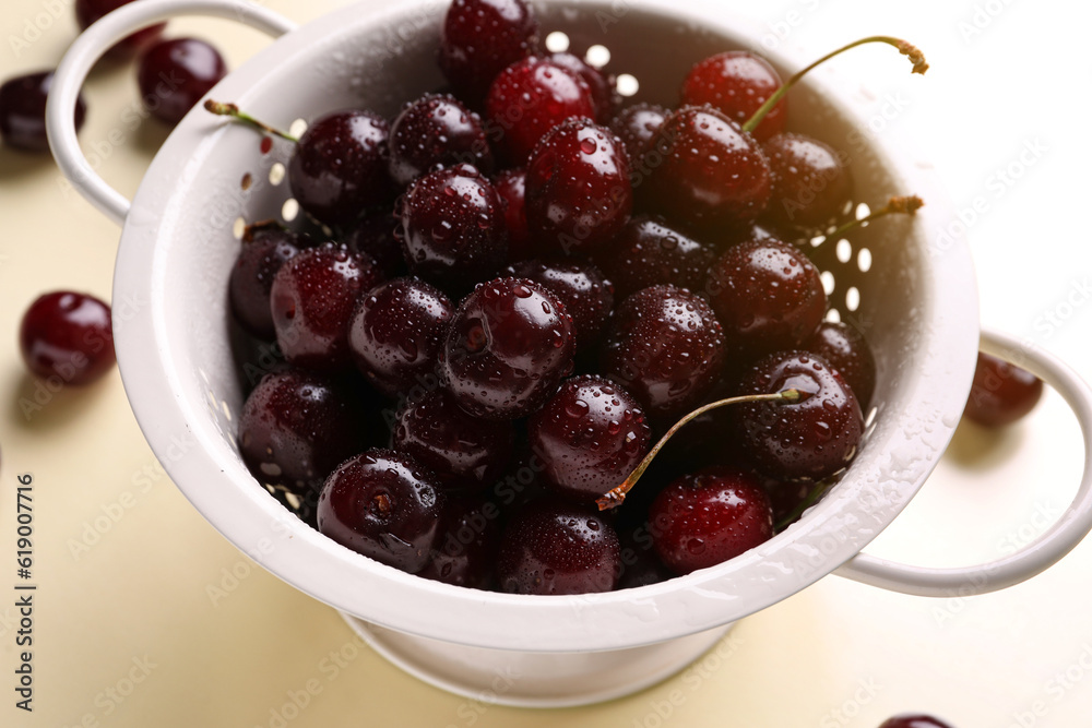 Colander with sweet cherries on beige background Colander with sweet cherries on beige background