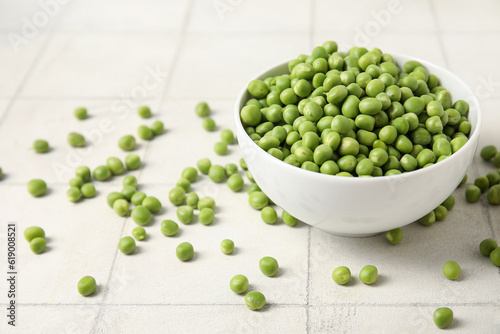 Bowl with fresh green peas on white tile background