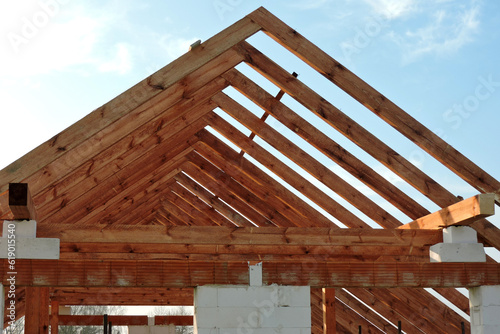 A timber roof truss in a house under construction, walls made of autoclaved aerated concrete blocks, rough window openings, a reinforced brick lintel, a scaffolding, blue sky in the background