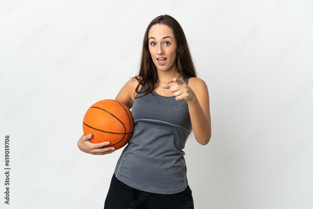 Young woman playing basketball over isolated white background surprised and pointing front