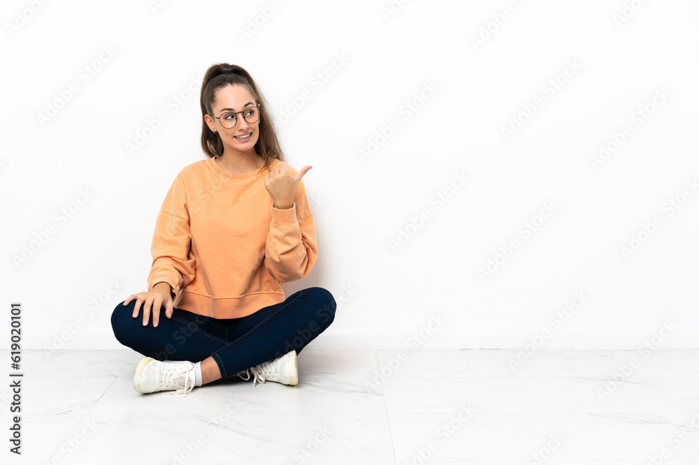 Young woman sitting on the floor pointing to the side to present a product Young woman sitting on the floor pointing to the side to present a product