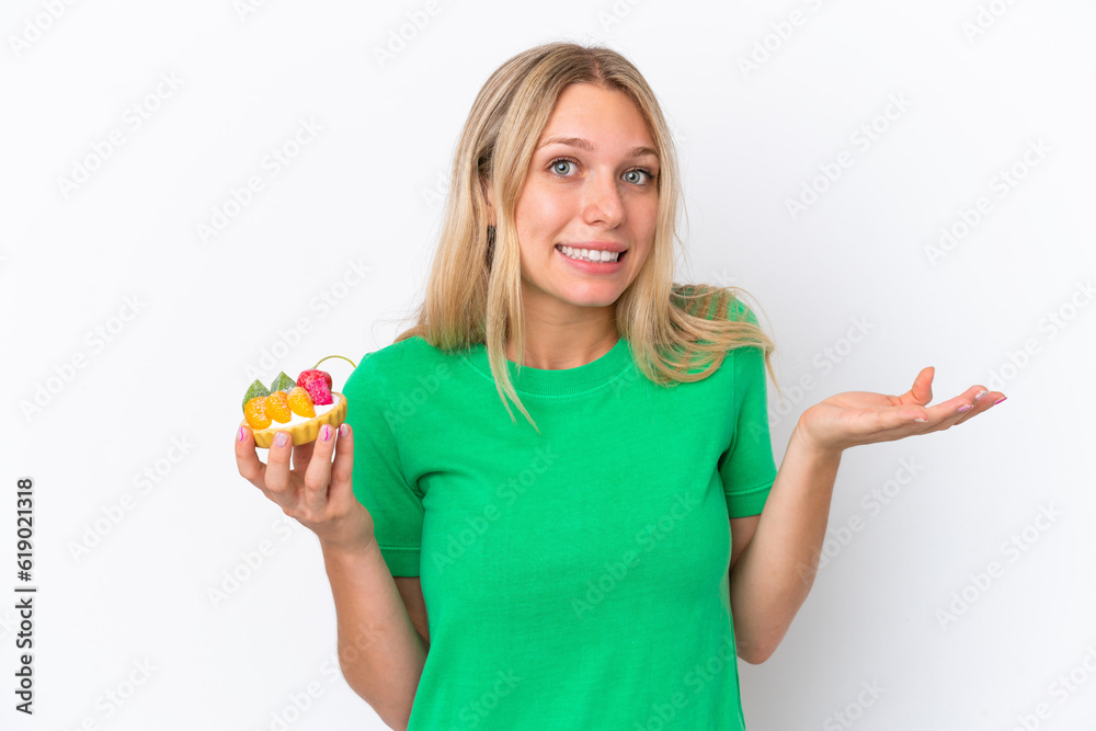 Young caucasian woman holding a tartlet isolated on white background having doubts while raising hands Young caucasian woman holding a tartlet isolated on white background having doubts while raising hands