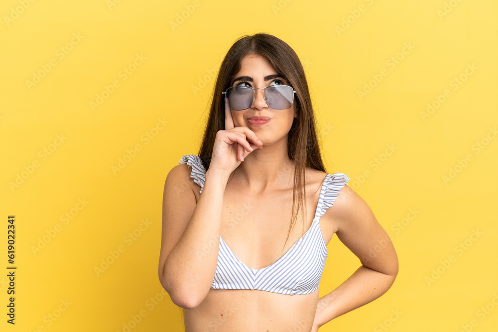 Young caucasian woman in swimsuit in summer holidays isolated on yellow background thinking an idea