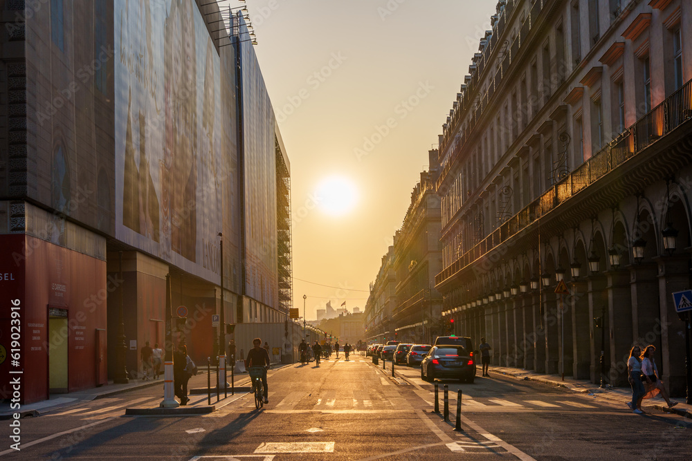 Obraz premium 夕日に照らされるパリの街並みと道路を行き交う車や通行人の交通