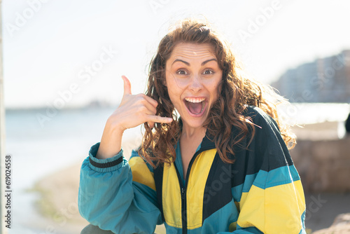 Young sport woman at outdoors making phone gesture. Call me back sign