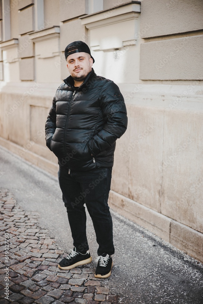 Obraz premium Portrait of a Caucasian man with a puffer jacket and a cap posing outdoors