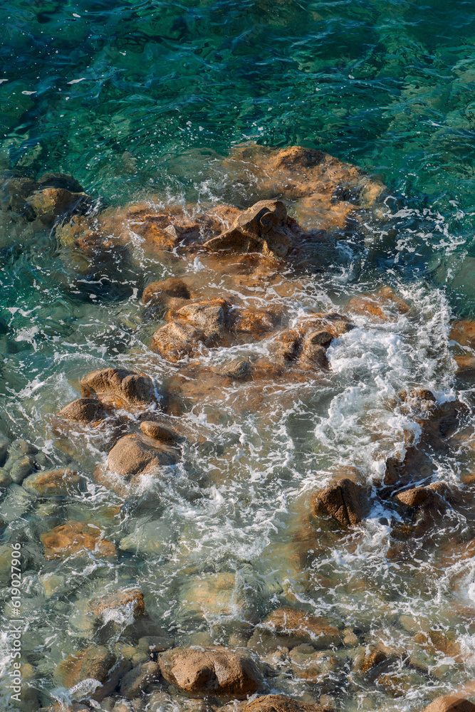 Waves on rocky beach, sea shore with waves crushing over the big rocks, summer sunny day Waves on rocky beach, sea shore with waves crushing over the big rocks, summer sunny day