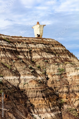 Jesus statue on the rocky hill of a valley in Drumheller with green grass on the eroded surface photo