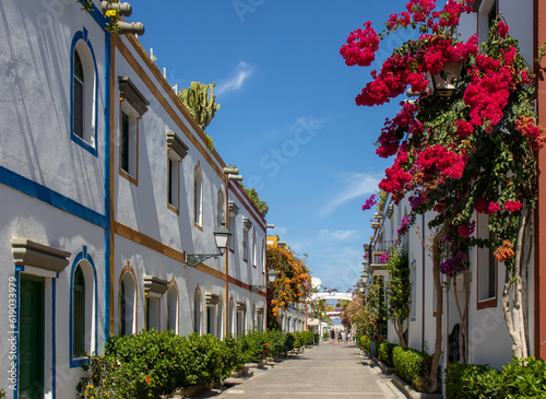 Street of Puerto de Mogán with its white houses with the frames of doors and windows painted in bright colors. Multiple bougainvillea and trees. Charming town, Gran Canaria, Spain