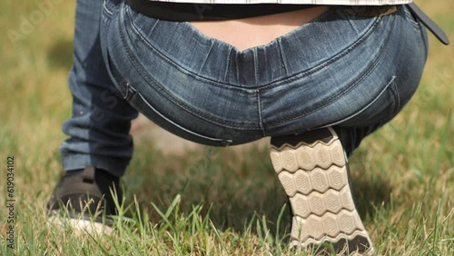 A woman in jeans squats and sits on a heel with her butt. sexy woman holding hands on her waist wearing blue jeans. Woman hand holding her bottom because having Abdominal pain