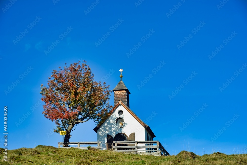 Postalm chapel in a field with a tree next to it in Salzkammergut, Austria