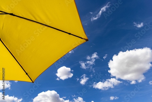 yellow umbrella and blue sky with clouds in the background from behind