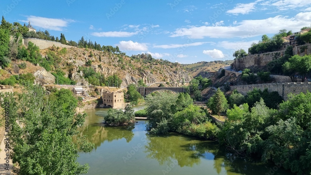 Scenic view of a large river surrounded by lush green hills in Toledo, Spain.