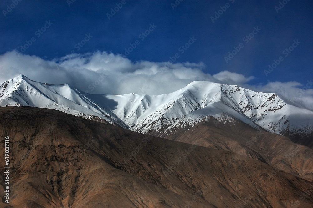 Landscape view with snowy Atlas mountains, cloudy and sunlit  sky background