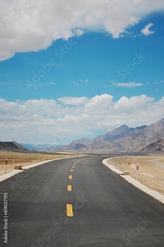Vertical of an empty highway alongside the wide field with big mountains in the background