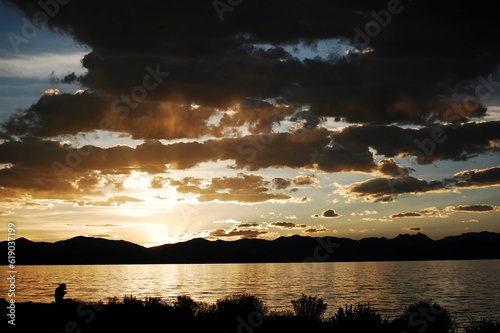 Golden sunset shining behind the silhouettes of mountains and the calm waters of the lake photo