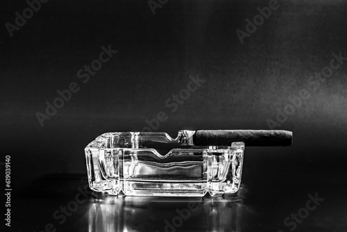 Empty glass ashtray with a single lit cigar placed on it