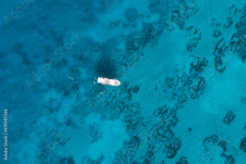 Aerial view of a yacht boat with vacationers and majestic blue sea with patterns on the bottom