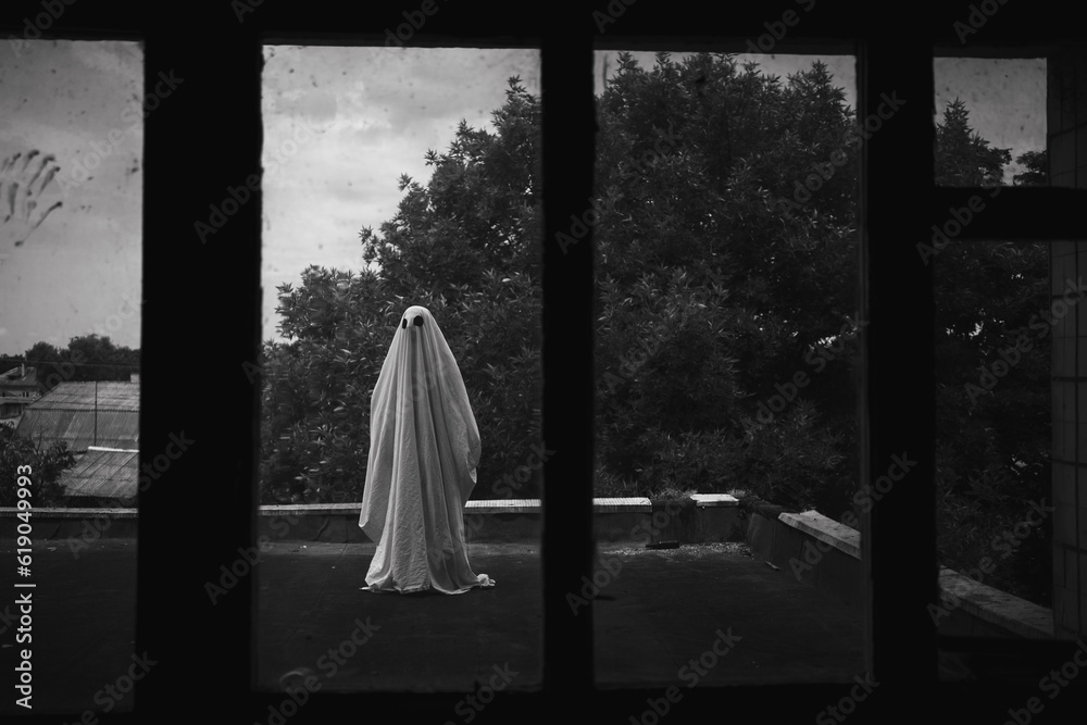 Ghost in a sheet on the roof of an old abandoned house view through the window, spooky Halloween concept Ghost in a sheet on the roof of an old abandoned house view through the window, spooky Halloween concept