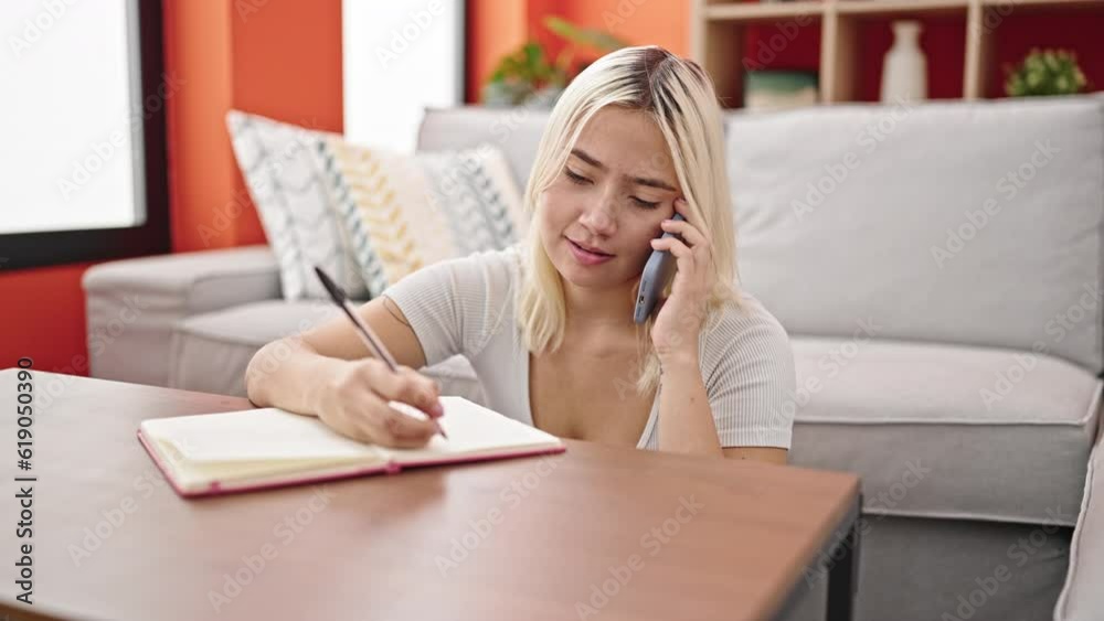 Young beautiful hispanic woman writing on notebook talking on smartphone at home Young beautiful hispanic woman writing on notebook talking on smartphone at home