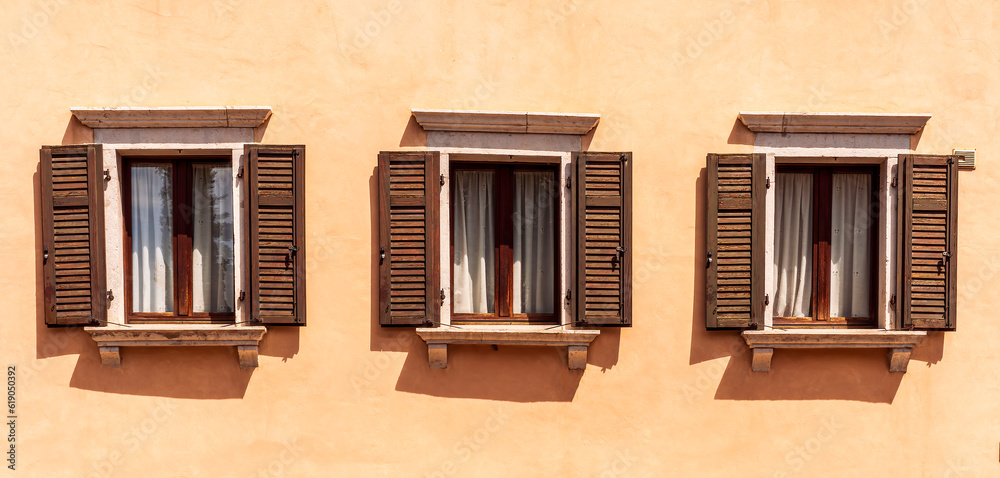 old yellow facade of house with three brown vintage wooden windows in retro italian european style