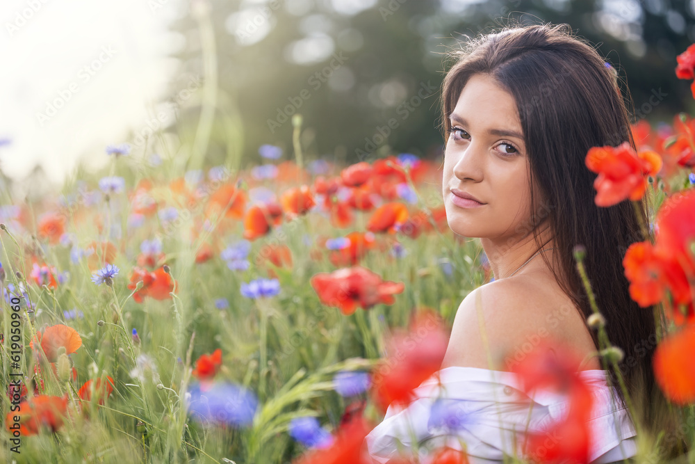 Naklejka premium Closeup side profile view of cool brunette girl exposing her shoulder sitting in red poppies and blue cornflowers meadow. 